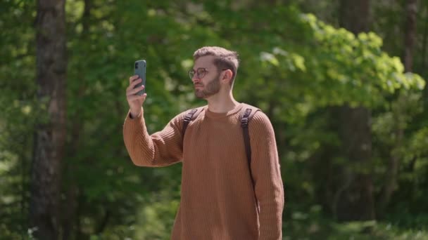 Muž turista pomocí smartphonu, zatímco si užívá víkend v lese. Nízký úhel pohledu na atraktivní muž batohem plánování cesty v lese na mobilním telefonu — Stock video