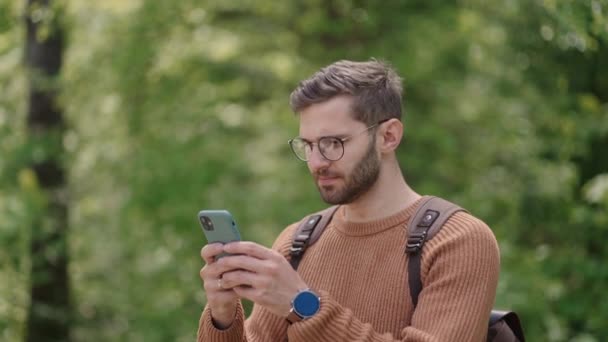 Man wandelaar met behulp van smartphone tijdens het weekend in het bos. Low angle view van aantrekkelijke man backpacker planning reis route in het bos op mobiele telefoon — Stockvideo