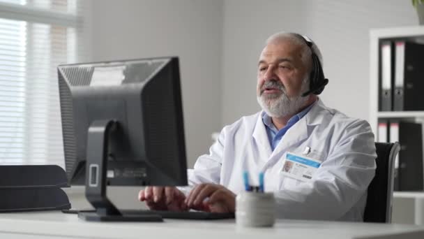 Medicine, technology and healthcare concept - senior male doctor or nurse with headset and computer working at hospital. Ambulance support hotline operator — Vídeos de Stock