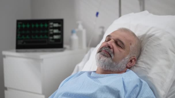 An elderly patient wakes up coming out of a coma. Open your eyes while lying on a bed in a hospital connected In the Hospital Sick Male Patient Sleeps on the Bed, . — Stok video