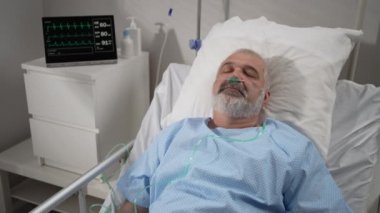 An elderly patient wakes up coming out of a coma. Open your eyes while lying on a bed in a hospital connected In the Hospital Sick Male Patient Sleeps on the Bed, .