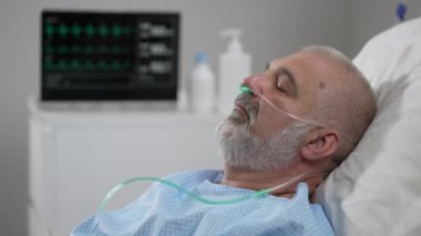 An elderly patient wakes up coming out of a coma. Open your eyes while lying on a bed in a hospital connected In the Hospital Sick Male Patient Sleeps on the Bed, .