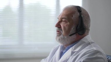 medicine, technology and healthcare concept - senior male doctor or nurse with headset and computer working at hospital. Ambulance support hotline operator