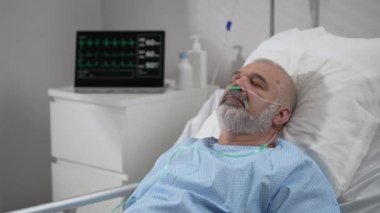 An elderly patient wakes up coming out of a coma. Open your eyes while lying on a bed in a hospital connected In the Hospital Sick Male Patient Sleeps on the Bed, .