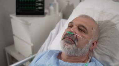 An elderly patient wakes up coming out of a coma. Open your eyes while lying on a bed in a hospital connected In the Hospital Sick Male Patient Sleeps on the Bed, .