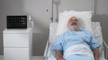 An elderly patient wakes up coming out of a coma. Open your eyes while lying on a bed in a hospital connected In the Hospital Sick Male Patient Sleeps on the Bed, .