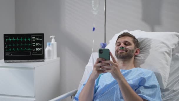 Man in hospital with the mobile phone and earphones lying alone in bed. Male Patient Using Mobile Phone In Hospital Bed — Stockvideo