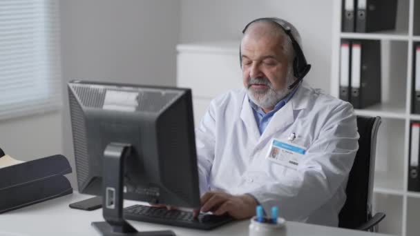 Medicine, technology and healthcare concept - senior male doctor or nurse with headset and computer working at hospital. Ambulance support hotline operator — Vídeos de Stock