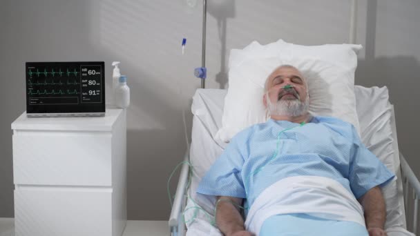 An elderly patient wakes up coming out of a coma. Open your eyes while lying on a bed in a hospital connected In the Hospital Sick Male Patient Sleeps on the Bed, . — Stock video