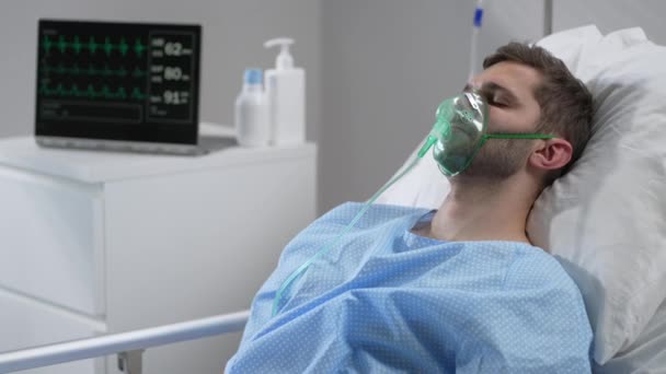 Caucasian man with oxygen mask on lying in bed with white linen, sleeping disturbingly, moving head. Portrait of a man in an oxygen mask who lies on a bed in a hospital. — Stockvideo