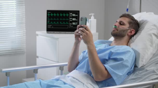 Man in hospital with the mobile phone and earphones lying alone in bed. Male Patient Using Mobile Phone In Hospital Bed — Stock videók