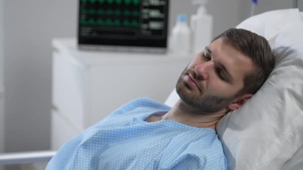 A young man lies on a bloodied hospital and opens his eyes. apparatus for monitoring heart, oxygen and pulse. A young patient of the clinic in a coma. Regain consciousness — Αρχείο Βίντεο