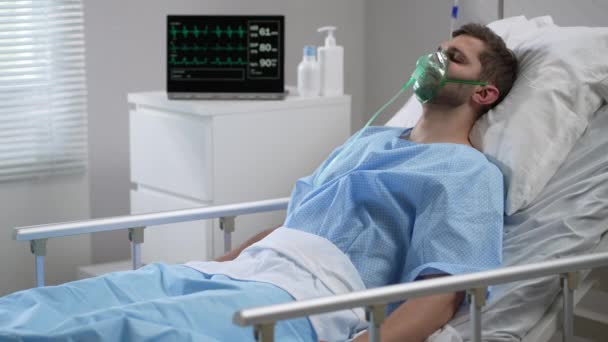 Caucasian man with oxygen mask on lying in bed with white linen, sleeping disturbingly, moving head. Portrait of a man in an oxygen mask who lies on a bed in a hospital. — Stockvideo