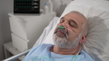 Senior male patient lying in a hospital bed wearing oxygen mask. The device shows the heart rate, pulse, oxygen in the blood, ecg