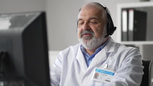 Medicine, technology and healthcare concept - senior male doctor or nurse with headset and computer working at hospital. Ambulance support hotline operator — Wideo stockowe