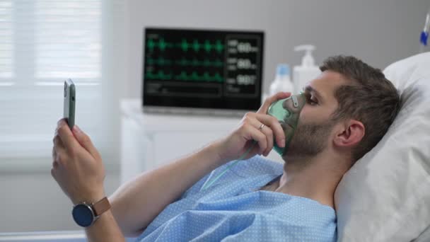 Man in hospital with the mobile phone and earphones lying alone in bed. Male Patient Using Mobile Phone In Hospital Bed — Stockvideo