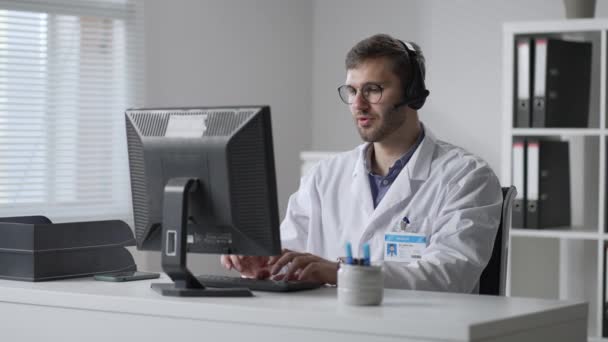 Male doctor or nurse with headset and computer working at hospital. Close up of medical operator with headphone consulting patients. Medical man operator working in a medicine call centre — 图库视频影像