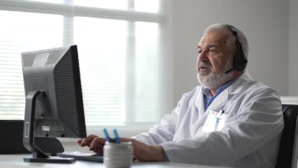 Docteur mâle assis à la table et utilisant un ordinateur portable. Homme en manteau blanc assis dans le bureau. — Video