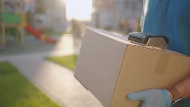 Eldivenli bir erkek teslimatçı bir kutu getiriyor ve satın almak için terminali veriyor. İçinde NFC kredi kartı ödeme terminali ya da cep telefonu olan bir kutu taşı. Temassız ödeme