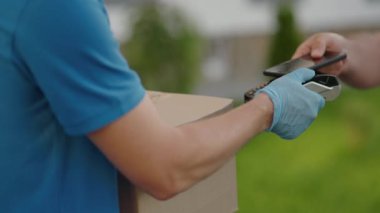 Temassız ödeme nfs sistemini kullanarak genç bir adamın teslimat eli satın almaları için ödeme yapıyor. Genç teslimatçı paketçi müşteri ödeme üniforması ekspres siparişi için telefonla ödeme yapıyor.