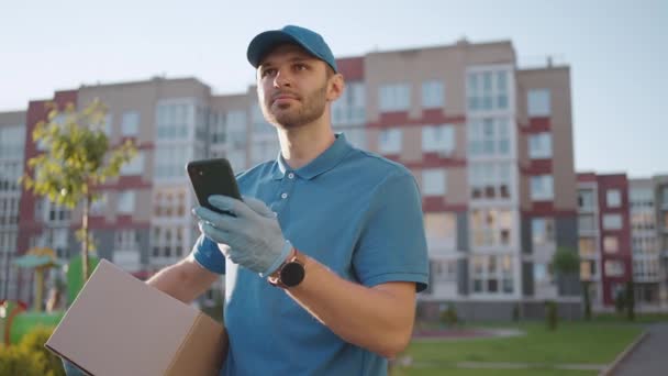 Erkek kurye bir dükkandan yiyecek teslimatı yapmak için cep telefonu arıyor. Teslimatçı adam şehirdeki telefonlarda dolaşıp teslimat adreslerini arıyor. Hızlı teslimat. — Stok video