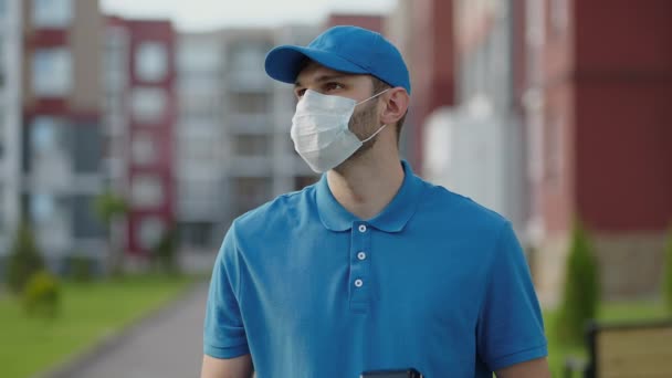 Een jonge koerier met een beschermend masker en handschoenen bezorgt een pakket direct bij een klant thuis met veiligheid. Concept van koerier, levering aan huis, e-commerce scheepvaart, virus, covid — Stockvideo