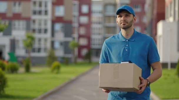 ブルー配達の男は荷物を配達する前に顧客にパッケージを送信します。4kの解像度とスローモーションショット。郵便配達の男が街の通りで小包を手に。郵便の概念。配達サービス. — ストック動画