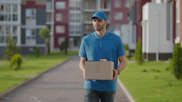 Blue delivery man send a package to customer on before deliver cargo. 4k resolution and slow motion shot. Male postman with parcel in hands at city street. Postal concept. Delivery service. — Stock Video