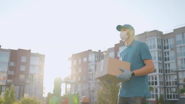 The male deliveryman in masks and protective gloves carries a parcel to the customer with a terminal for contactless payment by mobile phone or NFC card. — Stock Video
