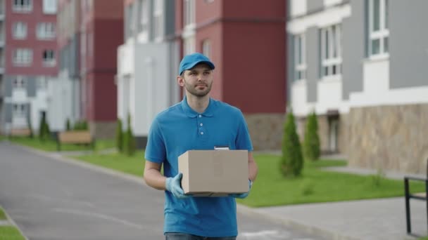 Чоловік синьої доставки відправляє посилку клієнту перед доставкою вантажу. Роздільна здатність 4k і повільний постріл. Чоловік листоноша з посилкою в руках на міській вулиці. Поштова концепція. Служба доставки . — стокове відео