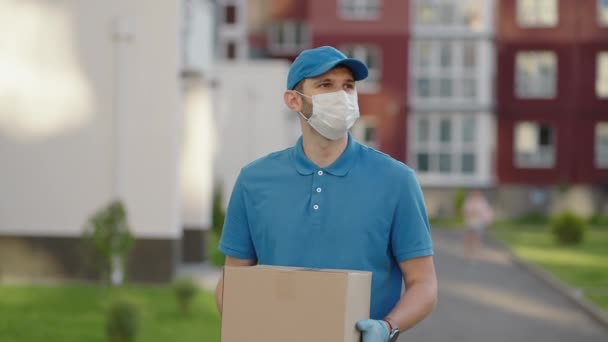 Ένας νεαρός ταχυδρόμος με προστατευτική μάσκα και γάντια παραδίδει ένα δέμα απευθείας στο σπίτι ενός πελάτη με ασφάλεια. Αντίληψη του courier, κατ 'οίκον παράδοση, e-commerce ναυτιλία, ιός, covid — Αρχείο Βίντεο