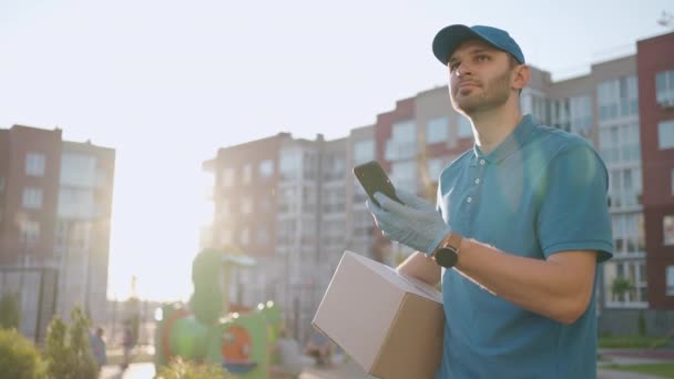 Mannelijke koerier man is op zoek naar mobiele telefoon om het adres van voedsel te leveren uit een winkel. Bezorger navigeert in de telefoon in de stad, op zoek naar winkelafleveradressen. Snelle levering — Stockvideo