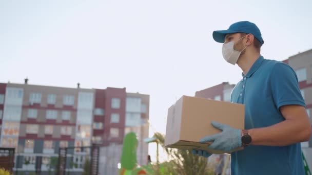 Koruyucu maskeli ve eldivenli genç bir postacı paketini güvenle bir müşteriye teslim ediyor. Kurye konsepti, ev teslimatı, e-ticaret nakliyesi, virüs, covid — Stok video