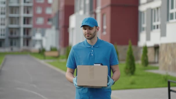 Blue delivery man send a package to customer on before deliver cargo. 4k resolution and slow motion shot. Male postman with parcel in hands at city street. Postal concept. Delivery service. — Stock Video