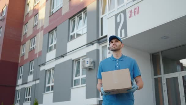 O homem azul da entrega envia um pacote ao cliente sobre antes de entregar a carga. Resolução 4k e tiro em câmera lenta. Carteiro com encomenda nas mãos na rua da cidade. Conceito postal. Serviço de entrega. — Vídeo de Stock