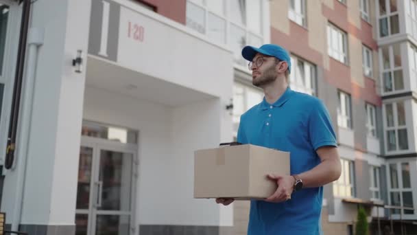 Jovem homem de entrega usando óculos e luvas segurando caixa usar telefone andando em quarentena rua pacote de compras ao ar livre pandemia carteiro auto isolamento câmera lenta — Vídeo de Stock