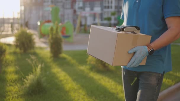 Un repartidor masculino en guantes trae una caja y le da a la terminal para pagar la compra. Lleve una caja con un terminal de pago con tarjeta de crédito NFC o un teléfono móvil. Pago sin contacto — Vídeo de stock