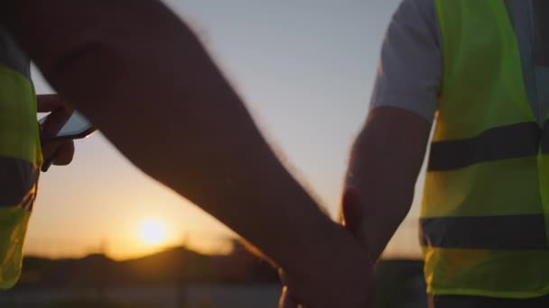 Portrait of hands of two builders. Builder shaking hand the builder on built house background. Close up of a handshake of two men in green signal vests against the background of the sun — Stok video