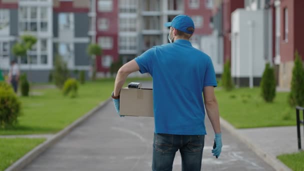 Een bezorger brengt een pakket naar klanten in een woonwijk. Boodschappenbezorging en online winkelen — Stockvideo