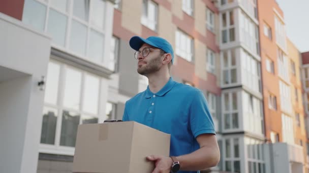 Un livreur transporte un colis aux clients dans un quartier résidentiel. Livraison d'épicerie et achats en ligne — Video