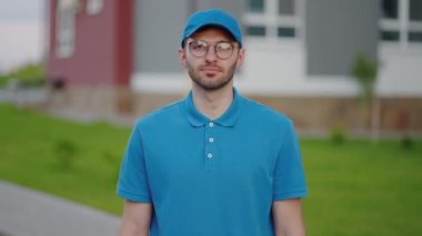 The happy delivery guy looks at the camera and smiles. Portrait of a delivery guy in slow motion. The postman with glasses smiles