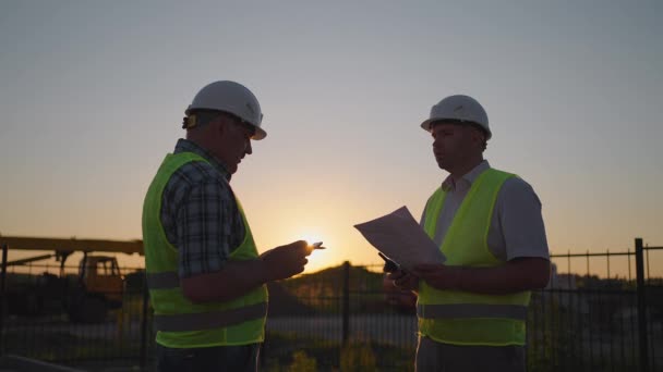 Portrait of hands of two builders. Builder shaking hand the builder on built house background. Close up of a handshake of two men in green signal vests against the background of the sun — Stockvideo