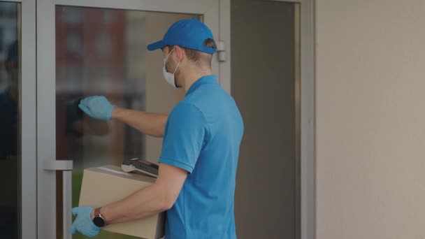 A delivery man wearing a protective mask and gloves passes the parcel to the customer and receives a contactless payment via NFC — Stock Video