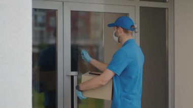 Pandemik ve çevrimiçi sipariş teslimatı koruyucu maskeli ve eldivenli bir teslimatçı pakedi müşteriye verir ve tas üzerinden ücretsiz ödeme alır.