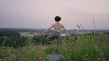 Dağların zirvesinde oturan barışçıl sporcu kadın zen, sağlık ve refah için temiz havanın tadını çıkarıyor. Aktif yaşam tarzı. Gün batımında dışarıda yoga yapan kadınlar yerlerinde oturuyorlar.