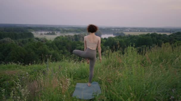 Meditación de yoga en montañas. Chica haciendo posturas de yoga, teniendo sesión de entrenamiento en el acantilado durante el amanecer. Mujer atlética joven meditando en la cima de una montaña, práctica de meditación de yoga zen en la naturaleza — Vídeos de Stock