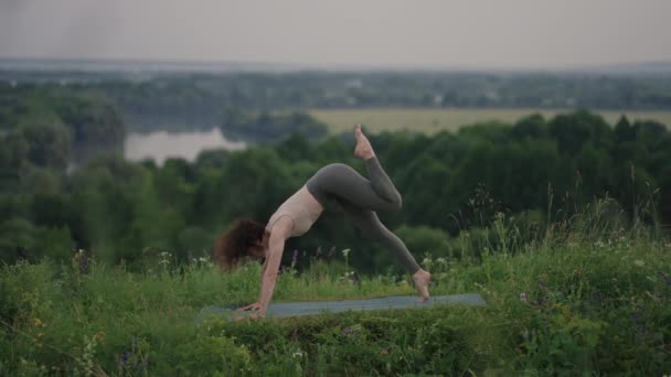 Dağların zirvesinde oturan barışçıl sporcu kadın zen, sağlık ve refah için temiz havanın tadını çıkarıyor. Aktif yaşam tarzı. Gün batımında dışarıda yoga yapan kadınlar yerlerinde oturuyorlar. — Stok video