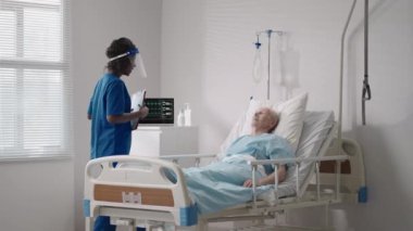 60-70 yaşlarında yaşlı beyaz bir adam hastane yatağında siyahi bir kadın doktorla konuşuyor. Bir kardiyolog nörologla tedavi tartışması. İyileşme sonrası rehabilitasyon planı