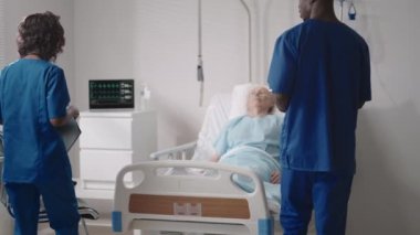 Yaşlı bir erkek hastanın yatağının yanında Afrikalı etnik tıp ekibine bakmak. Bakım görevlileri yaşlı bir erkek hastane hastasının hayati belirtilerini izliyor.