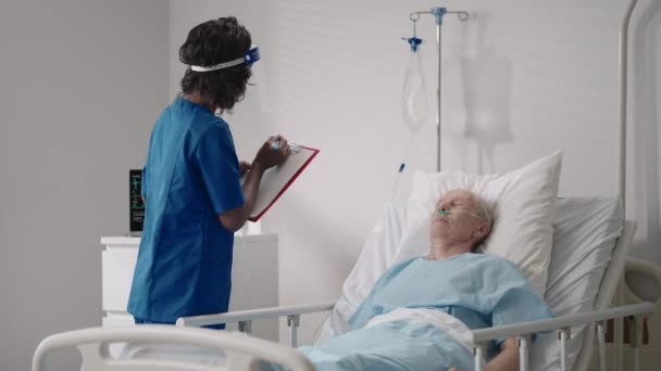 Černoška kardioložka mluví se starým mužem, který leží na nemocničním lůžku a probírá rehabilitaci po uzdravení. infekční neurologové diskutují o léčebné strategii — Stock video